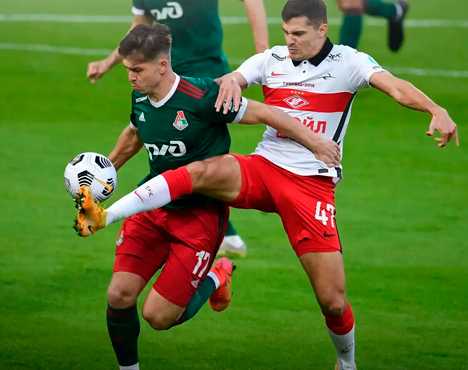 Два футболиста сражаются за мяч на поле. Один в форме зеленого цвета, второй — в бело-красной. Игрок в зеленой форме пытается контролировать мяч, противостоя сопернику, который активно мешает ему